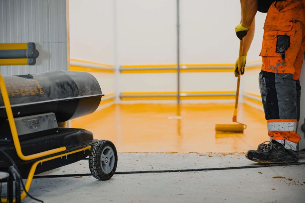 The man carefully applies a coating of yellow epoxy paint onto the floor using a roller brush.